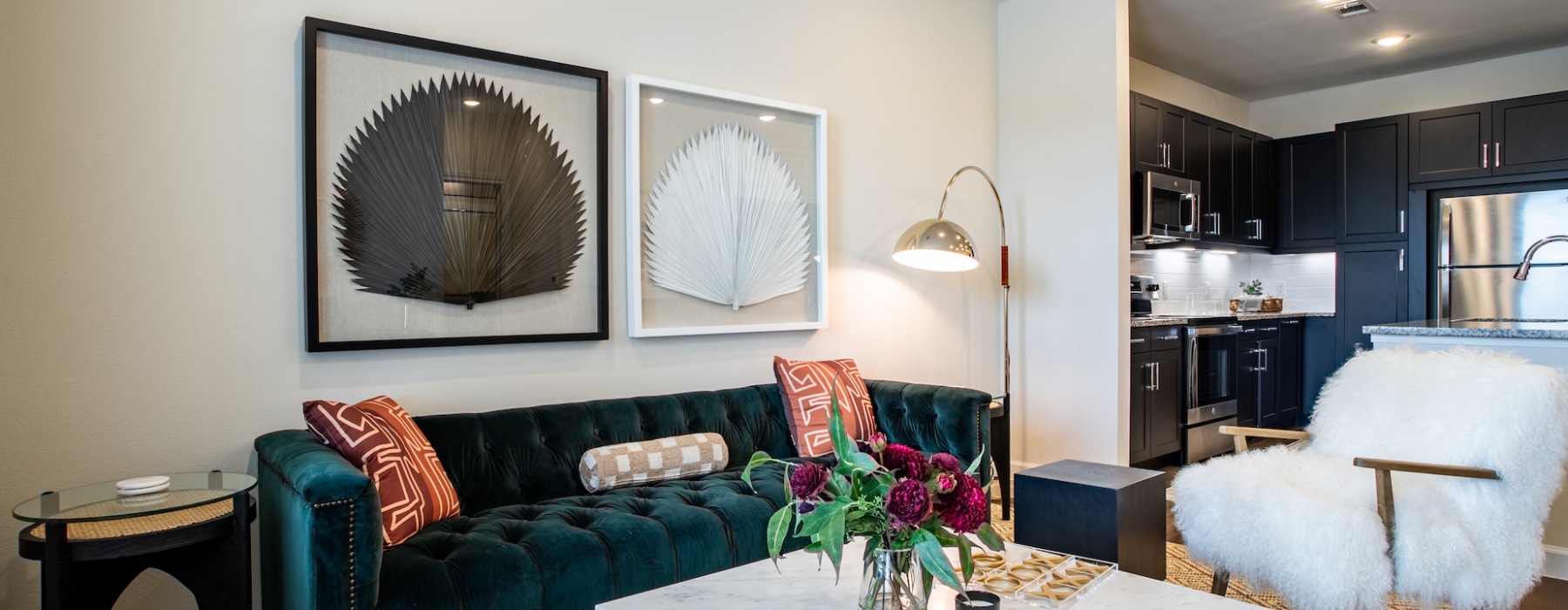 Living room with a couch, chair, coffee table, and views of a kitchen with black cabinets and stainless steel appliances in a 1 bedroom apartment in Richmond, Texas at West End.