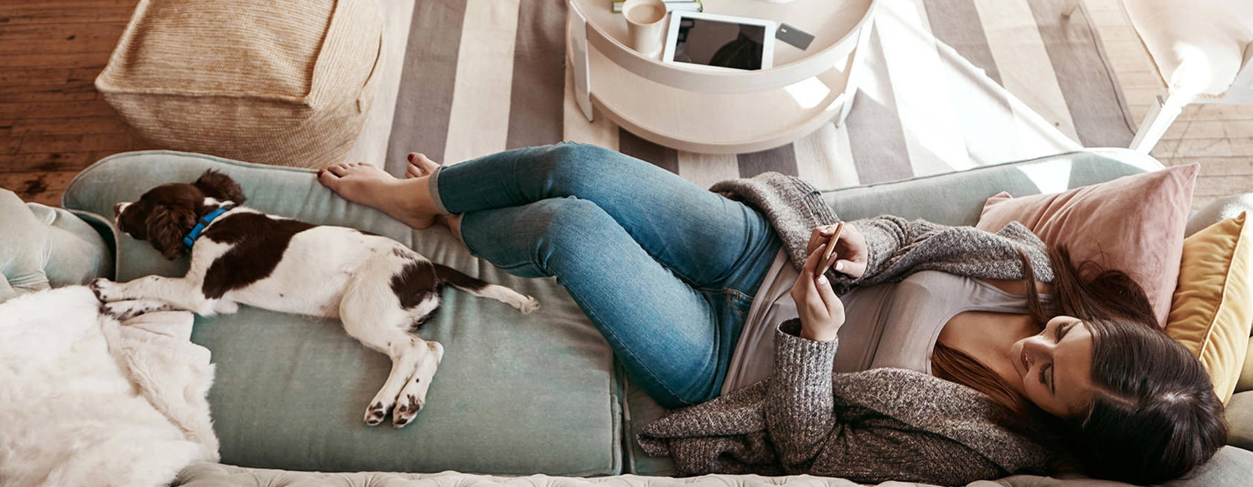 woman relaxing with dog on couch while playing on her phone