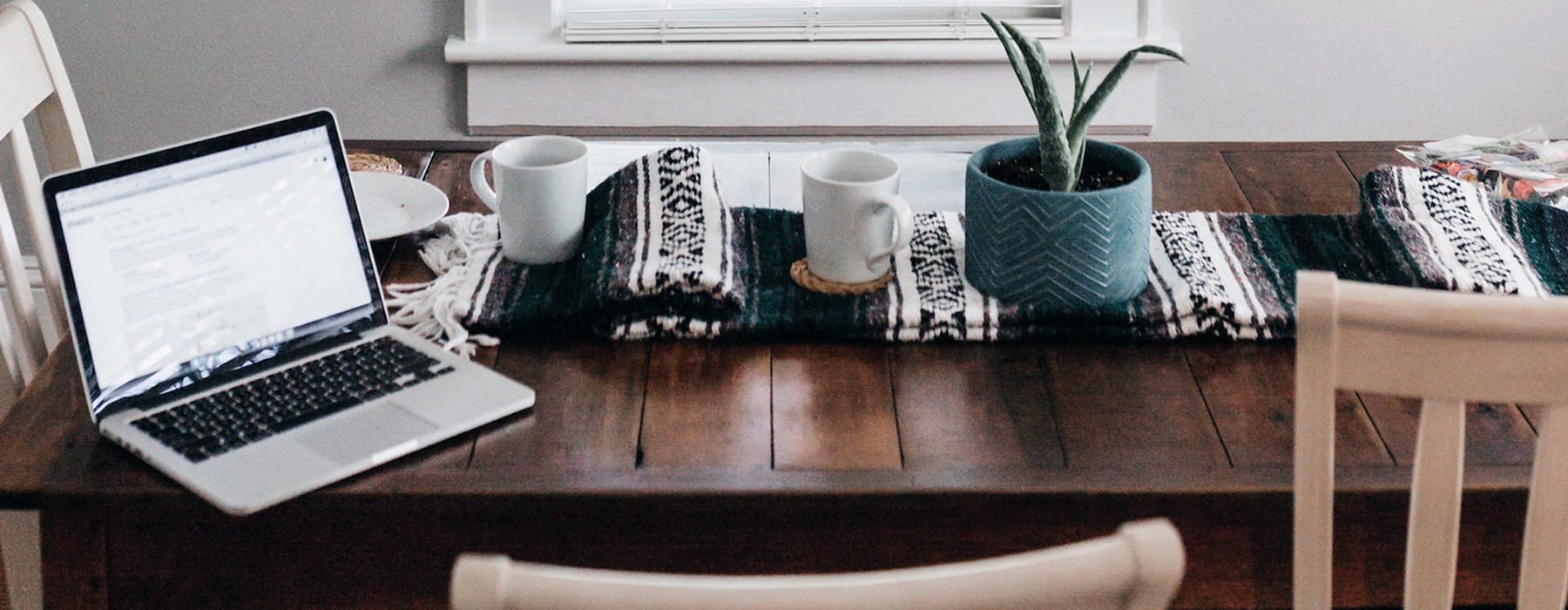 cozy table with computer and coffee mugs, plant, and blanket